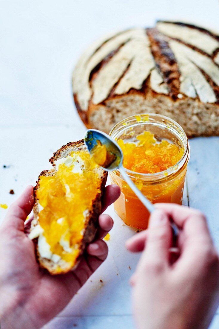 Person spreading pumpkin and orange jam on a slice of bread