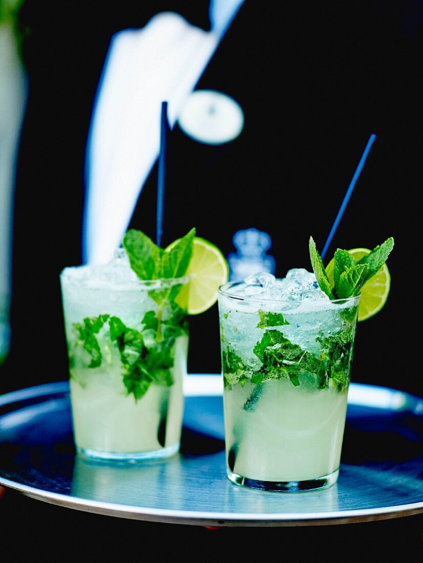 Waiter carrying a tray with two glasses of vodka mojito