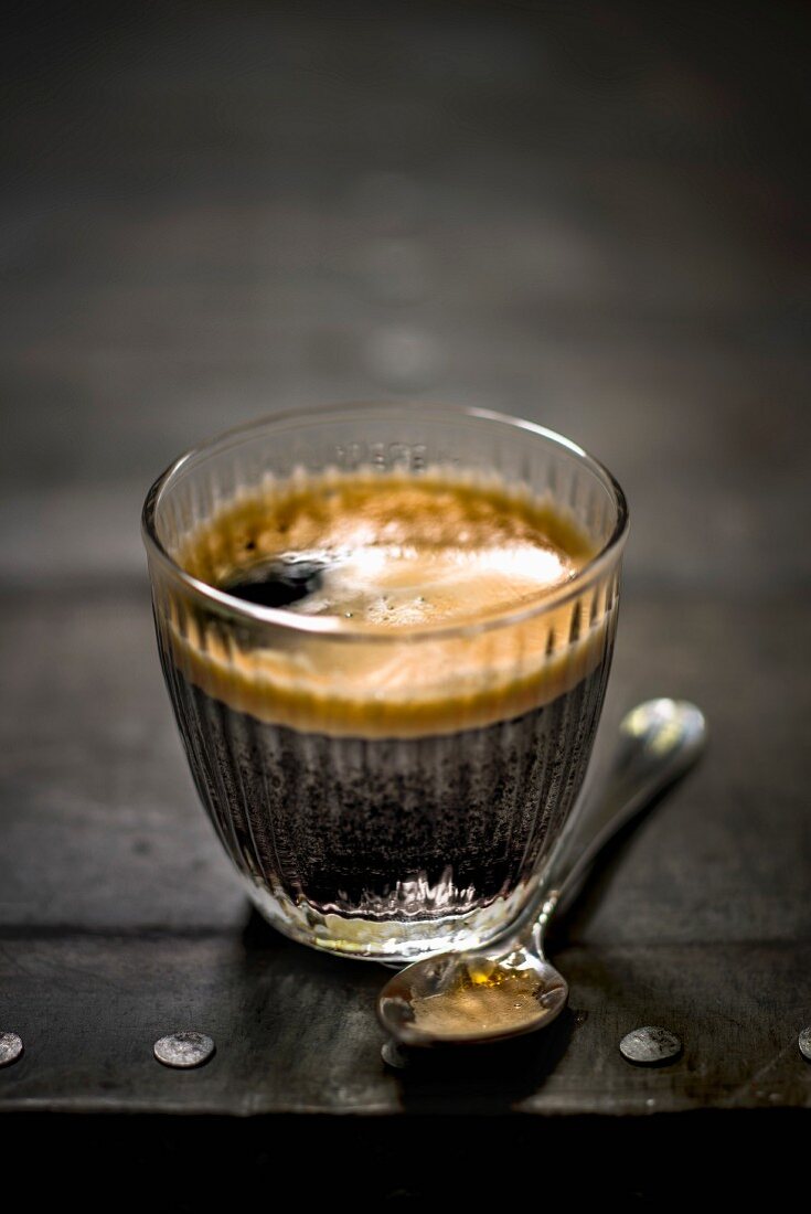 Espresso im Glas und Löffel auf schwarzem Untergrund