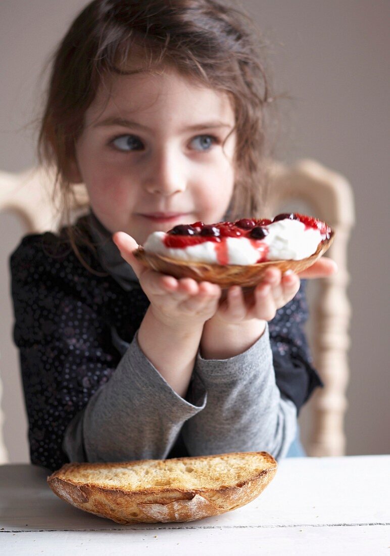 Kleines Mädchen hält eine Brotschnitte mit Frischkäse und Waldfrüchten