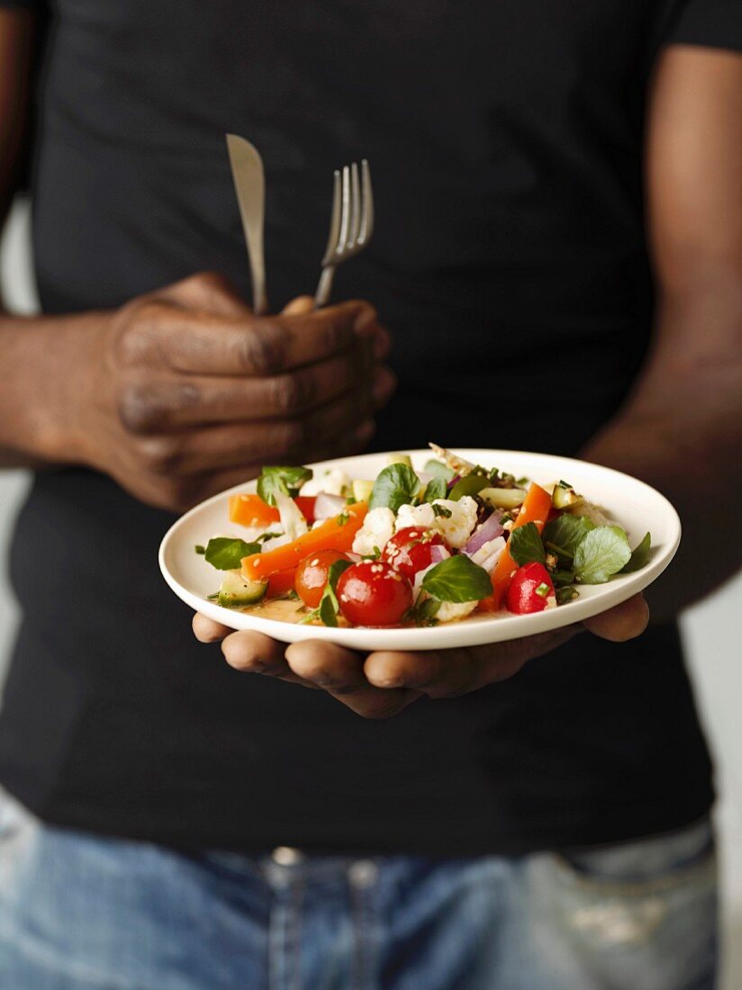 Person holding a plate of watercress and mixed vegetable salad