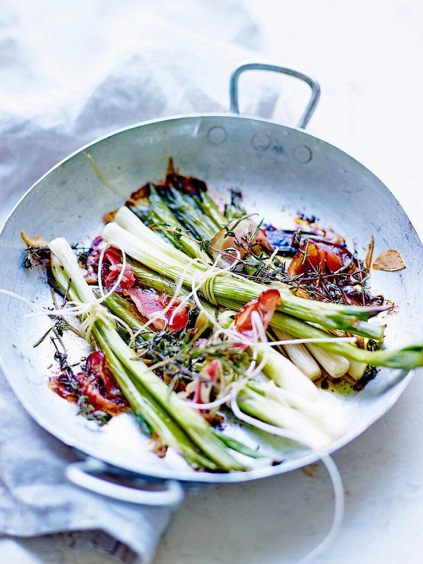 Bundles of spring onions with thyme and bacon