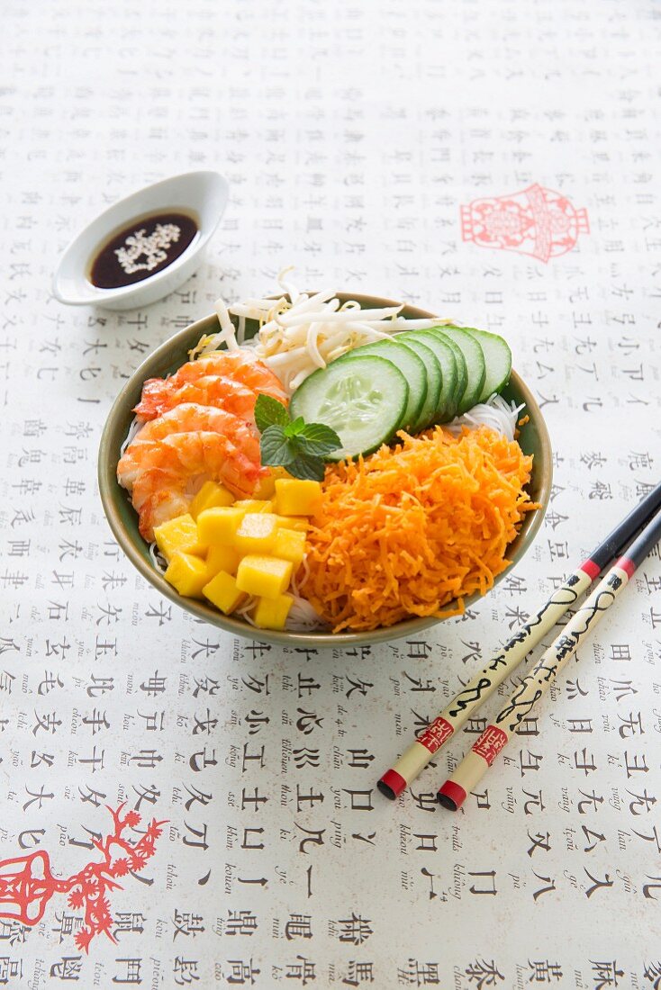 Asiatische Buddha Bowl mit Reisnudeln, Karotten, Mango, Gurke, Garnelen und Sojasauce