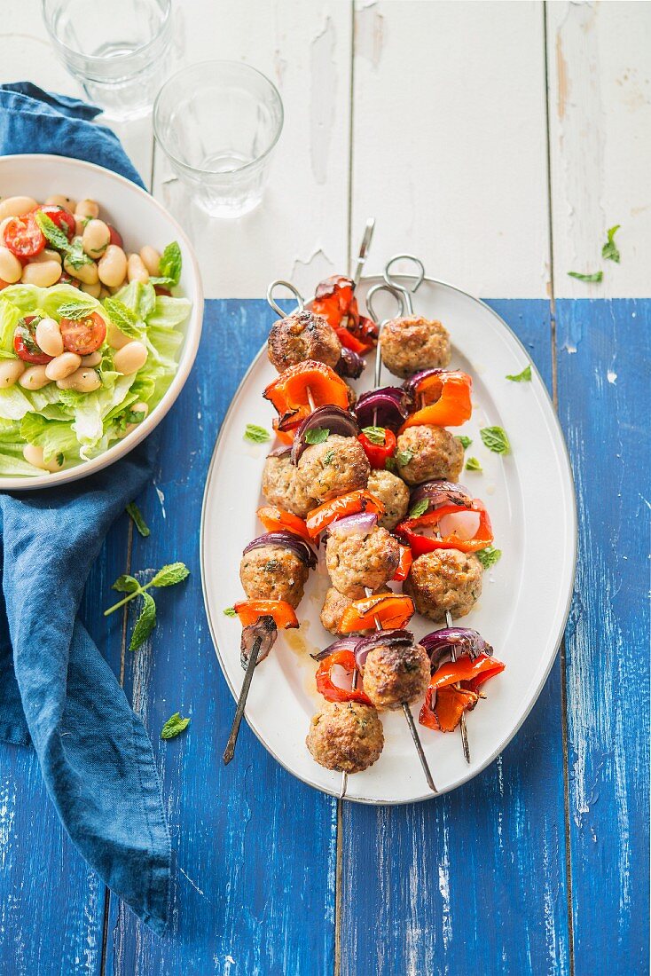 Meatball, onion and pepper skewers, white haricot bean and tomato salad