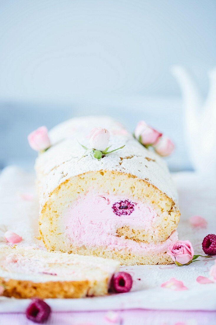 Rolled sponge cake garnished with raspberries and rose