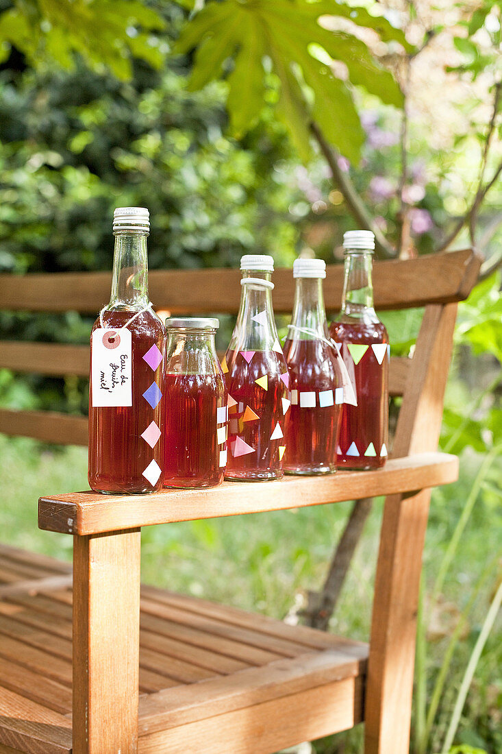 Homemade fruit juice with honey in glass bottles on the armrest of a garden bench