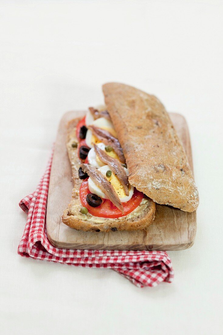 Biobrot-Sandwich mit Tomaten, Oliven, hartgekochtem Ei, Kapern und Sardellen