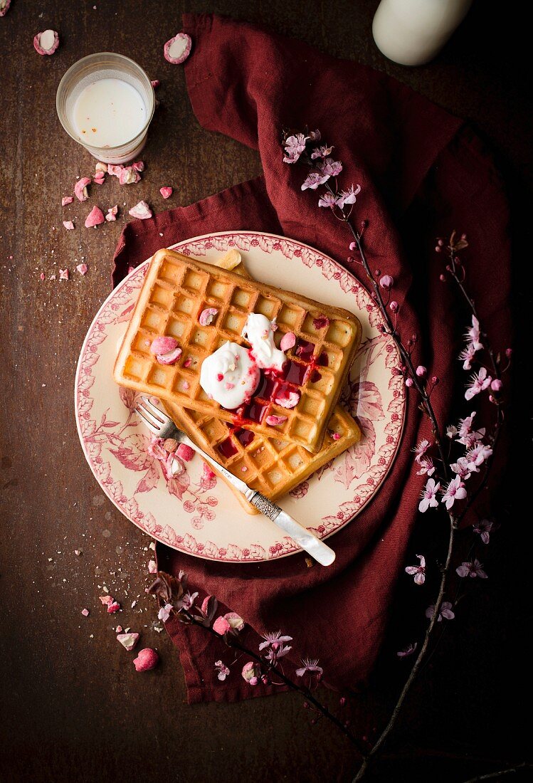 Pile of plain Brussels waffles with red berry coulis, cream and pink pralines