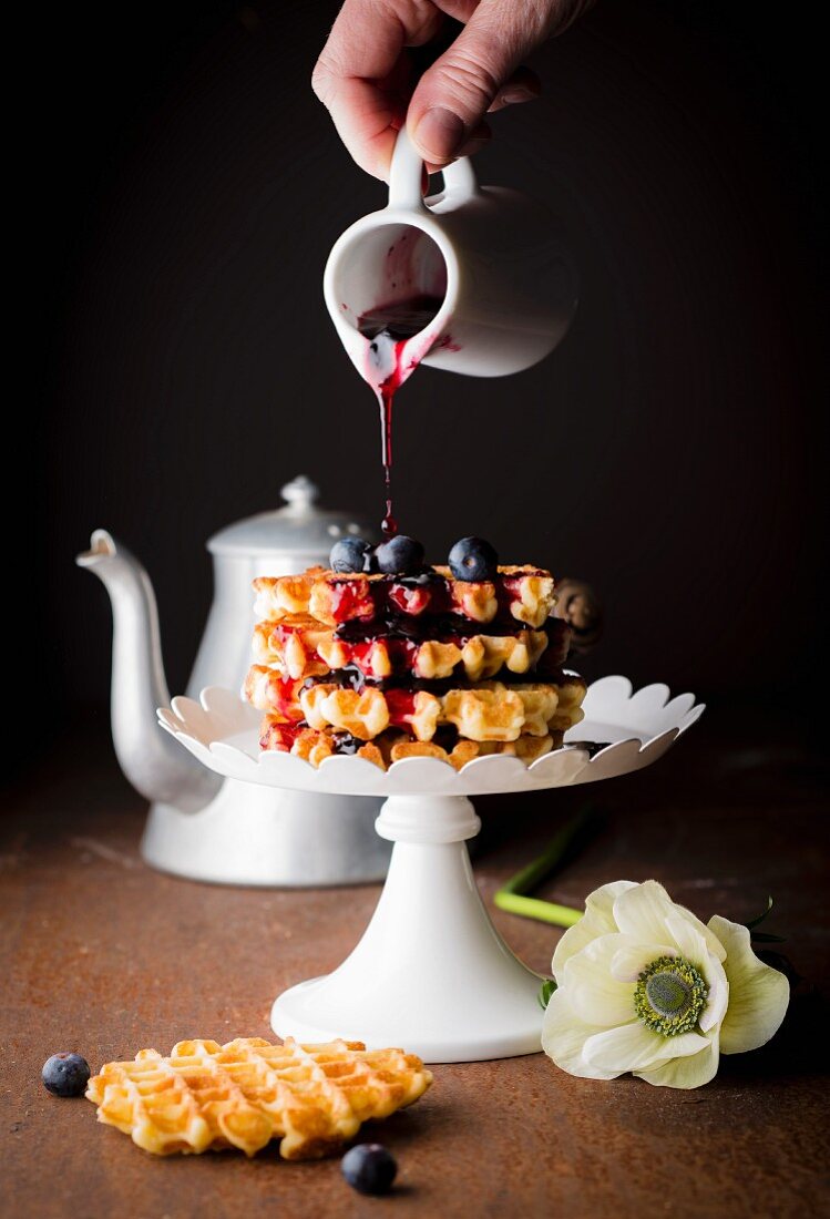 Pouring blueberry coulis onto a pile of waffles Liégeoises