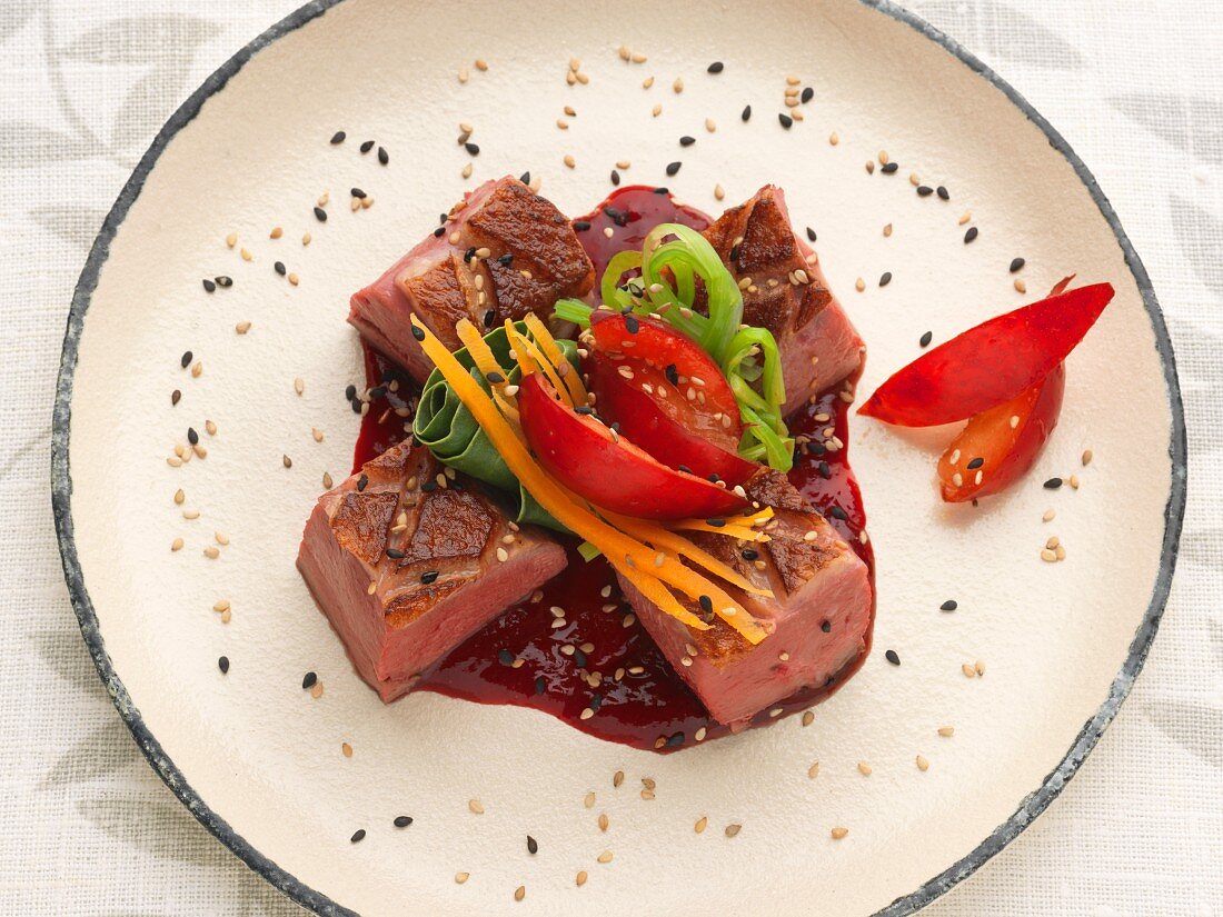 Duck breast with black and golden sesame seeds, cranberry sauce, plums and spring vegetables