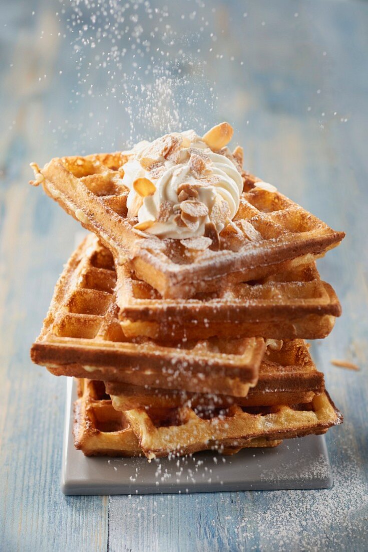 Sprinkling icing sugar onto the waffles from Brussels with whipped cream and almonds