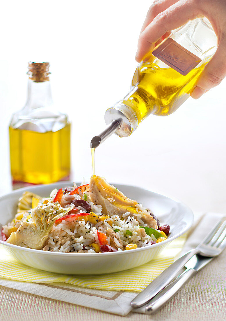 Pouring olive oil on a rice, sweet corn, artichoke, pepper and red kidney bean salad