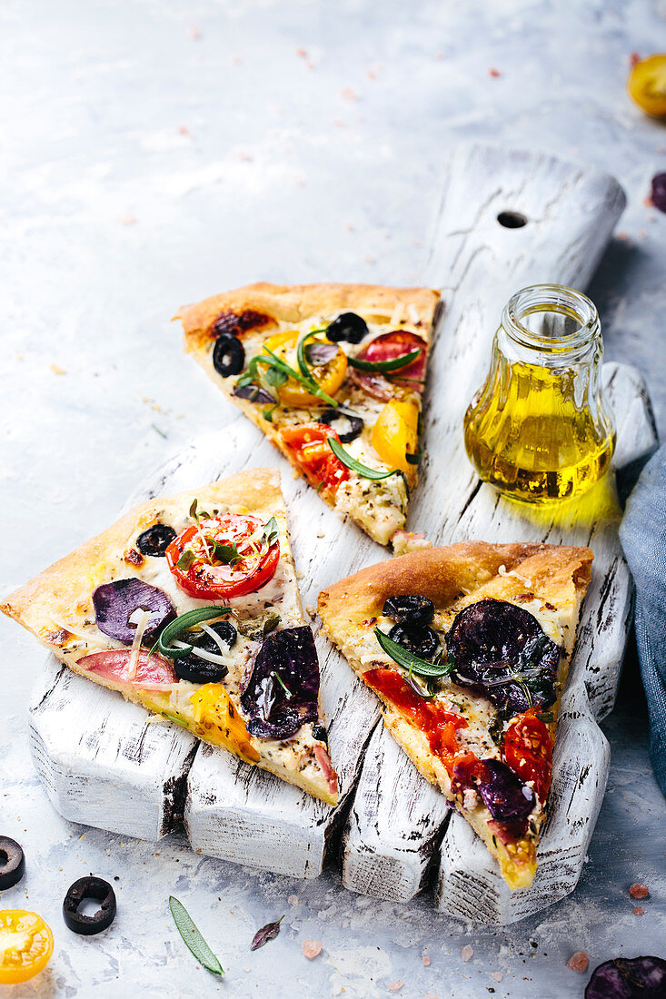 Drei Stücke vegetarische Pizza mit roten und gelben Tomaten, Rosmarin, Oliven und violetten Kartoffeln