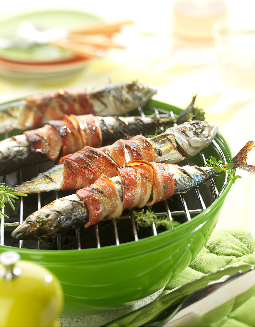 Mackerels with thyme and bay leaves wrapped in smoked bacon on the barbecue