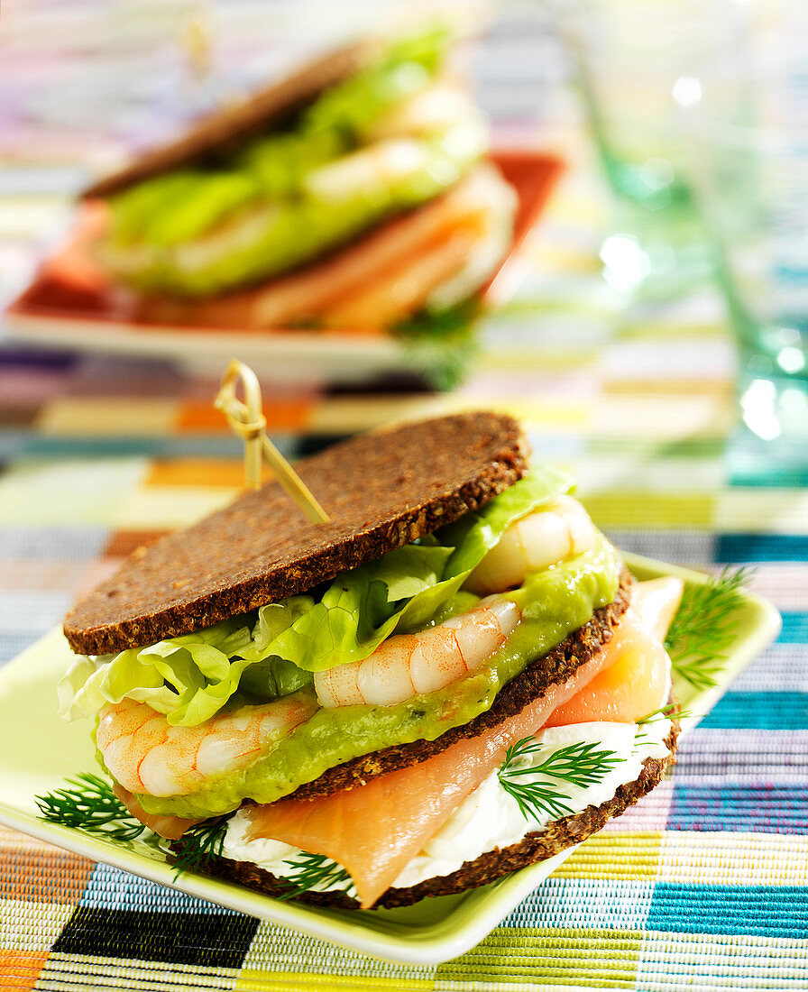 Nordisches Schwarzbrot-Sandwich mit Frischkäse, Räucherlachs, Garnelen und Guacamole