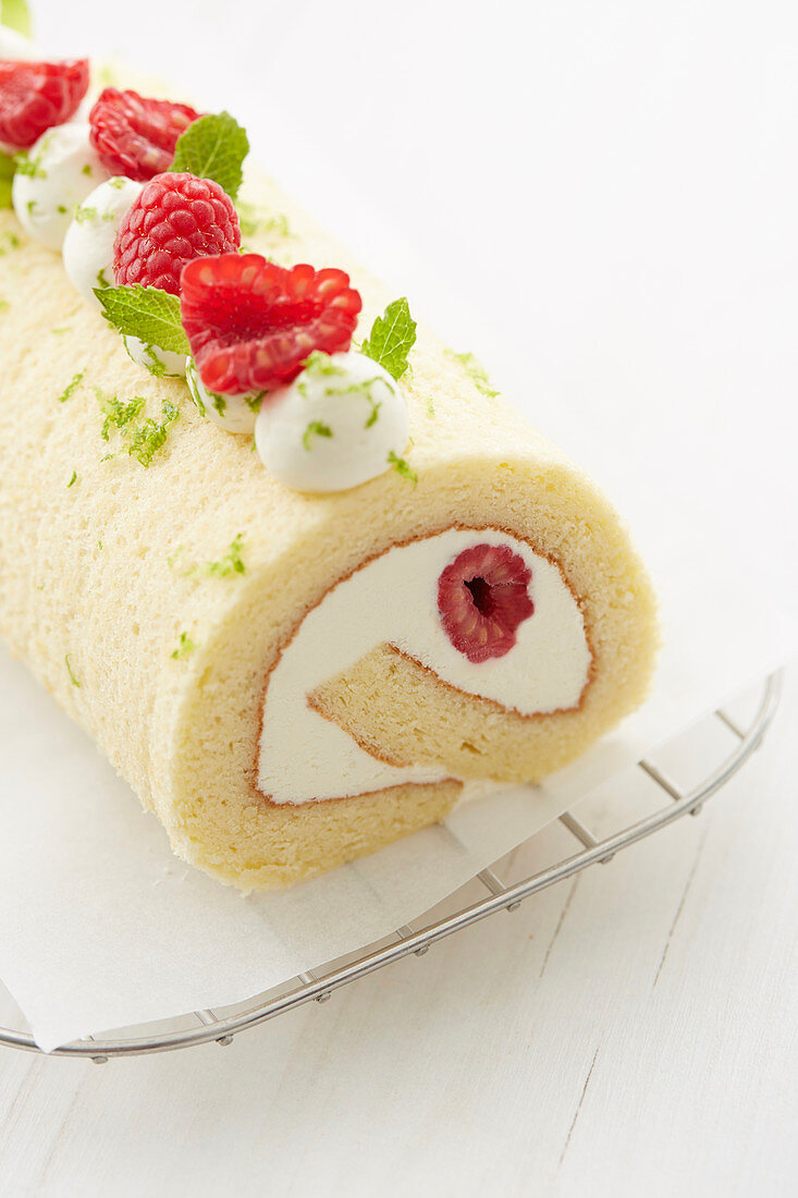 White chocolate and raspberry rolled sponge cake decorated with raspberries, lime zests and mint