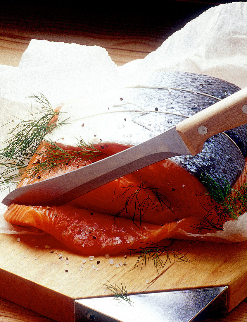 Slicing raw salmon marinated with dill