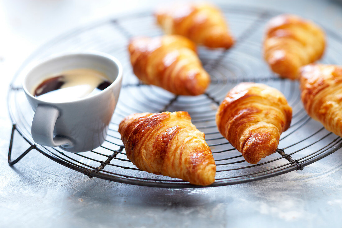 Butter croissants on a baking rack and a cup of coffee