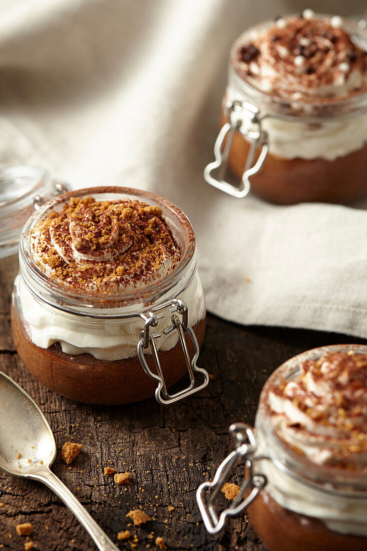Jars of chocolate mousse with whipped cream topped with cocoa and spicy biscuit crumbs