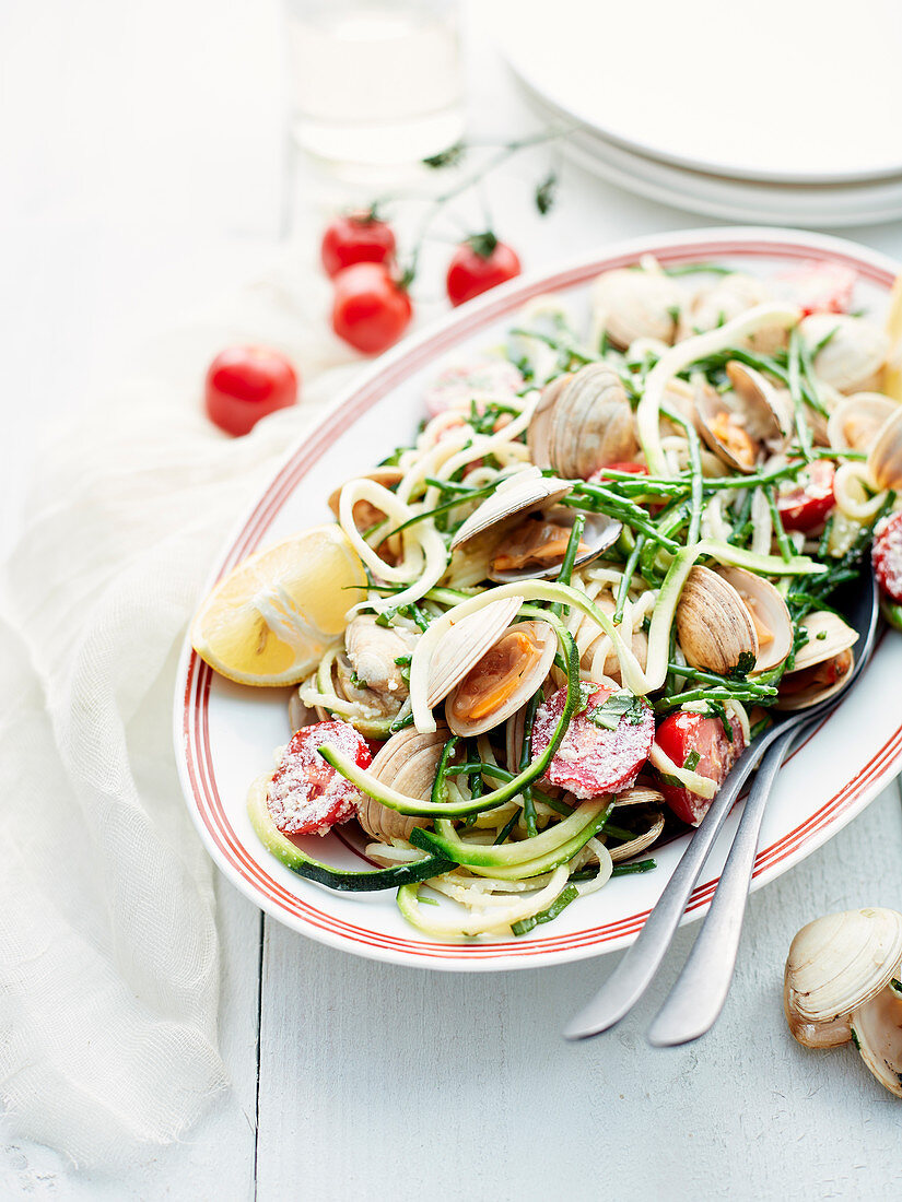 Spaghetti with clams, salicornia, zucchini strips, tomatoes and lemon