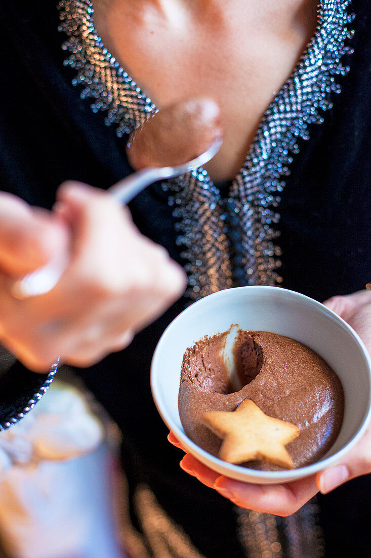 Woman tasting a bowl of chocolate mousse and star-shaped biscuit
