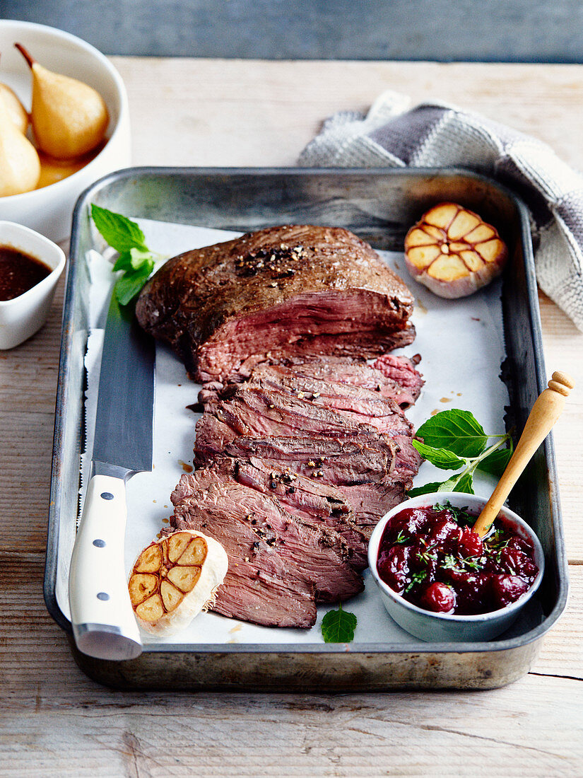 Deer roast with pepper and cranberry sauce,roasted garlic heads and poached pears