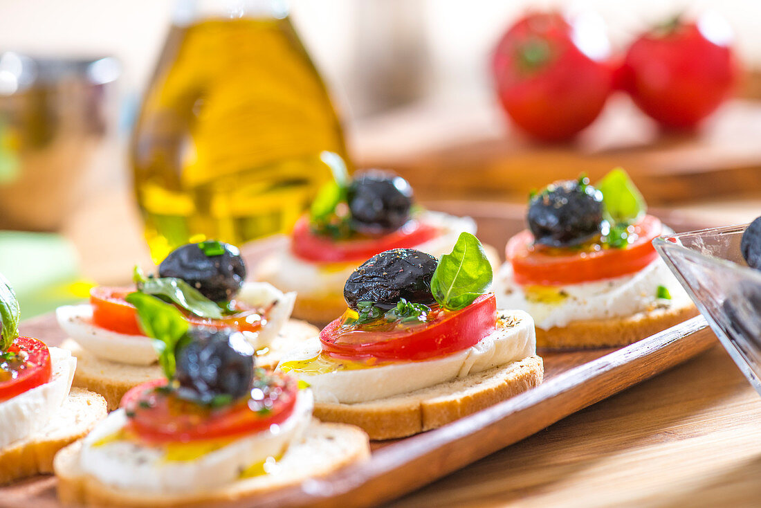 Belegte Brote mit Tomate, Mozzarella und Olive auf einem Tablett