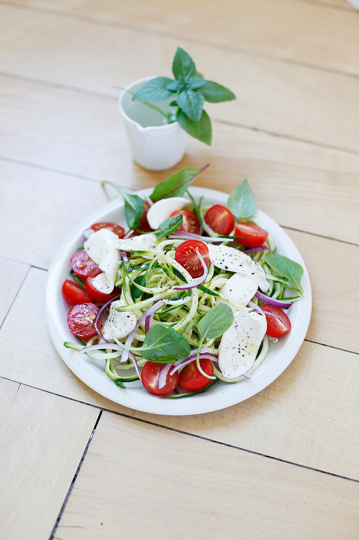 Salat mit Zucchinistreifen, Kirschtomaten, Mozzarella, roten Zwiebeln und Basilikum