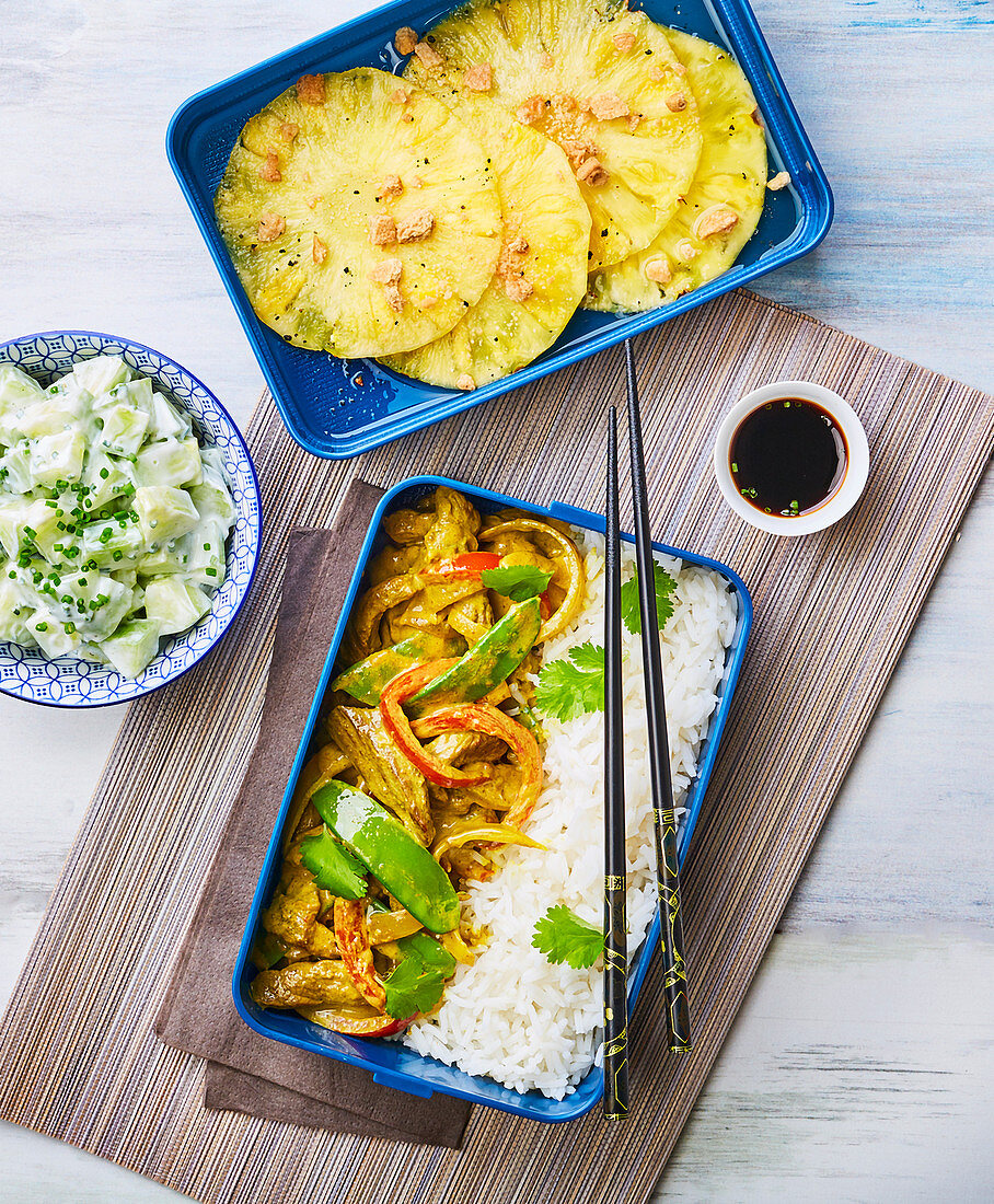Thai curry with rice and fried pineapple slices in lunch boxes
