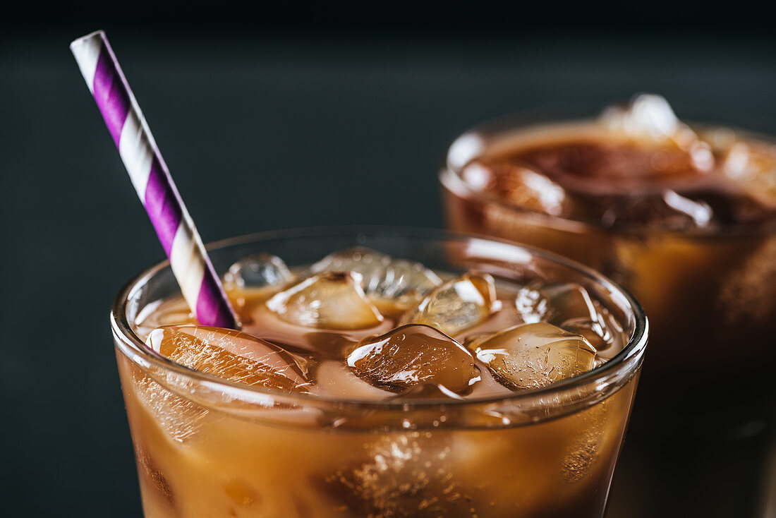 Glass of cold iced coffee with straw on dark background