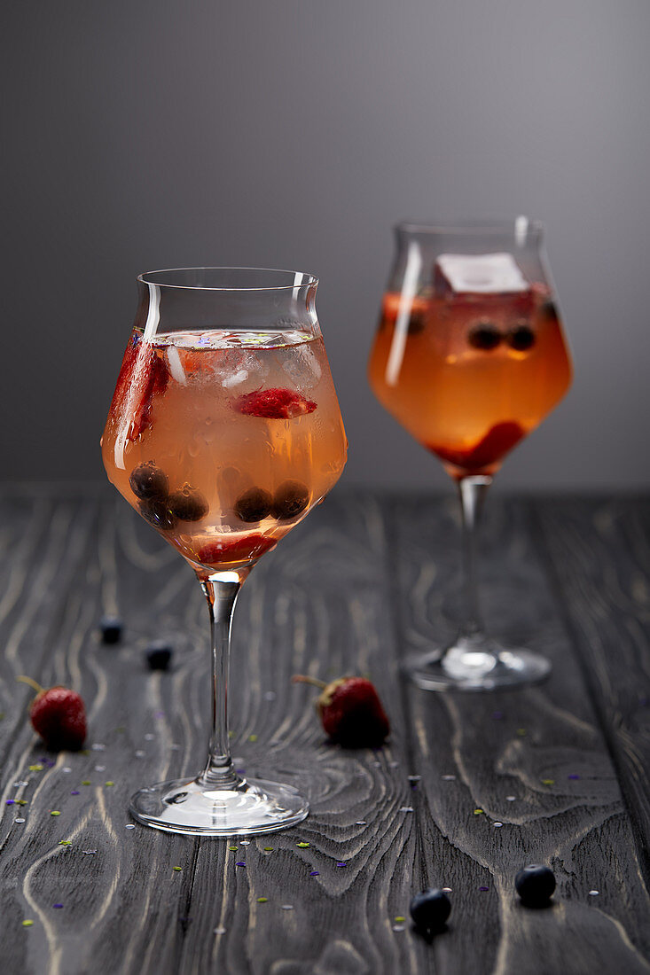 Two glasses of lemonade with ice cubes, strawberries and blueberries on grey background