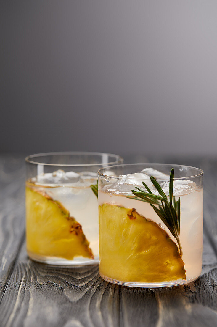 Two glasses of lemonade with pineapple pieces, ice cubes and rosemary