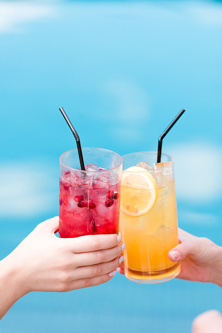 Hände beim Anstoßen mit zwei Cocktails am Swimmingpool