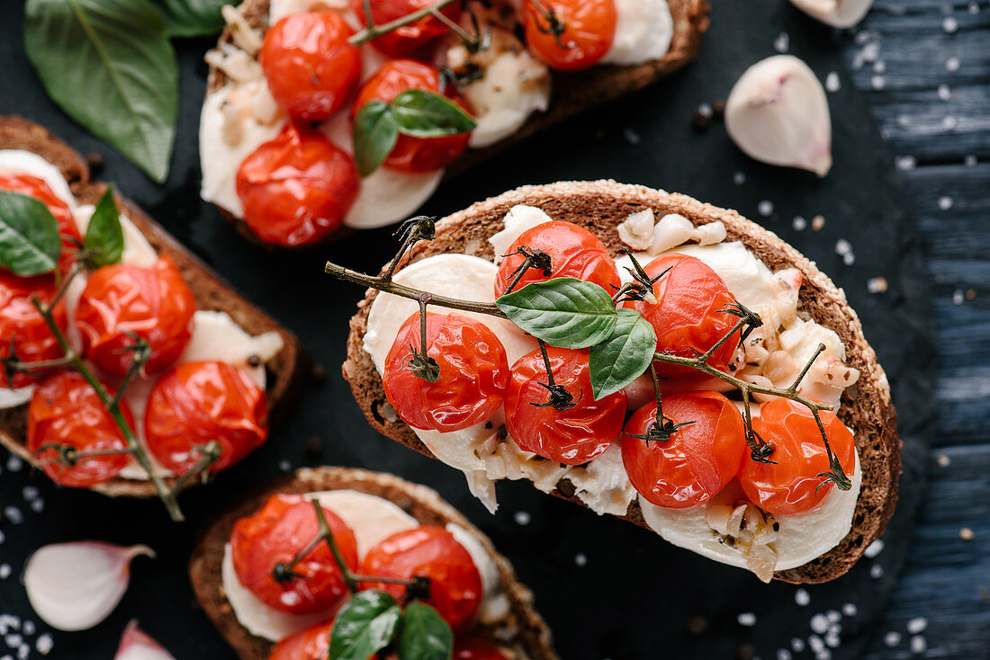Delicious sandwiches with mozzarella and baked tomatoes on dark wooden table