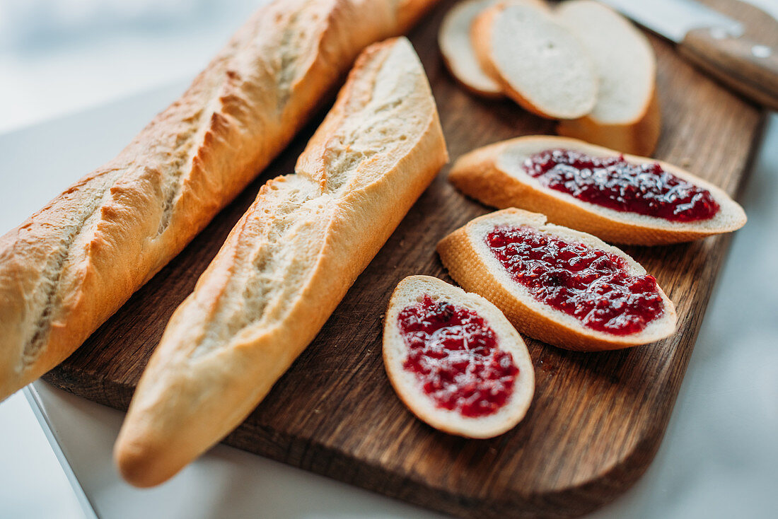 Sliced baguette with jam on wooden cutting board