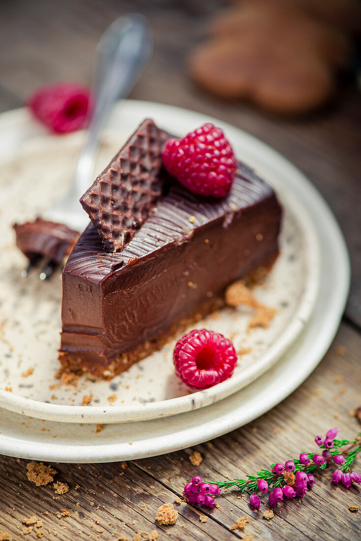 Slice of chocolate truffle cake with ginger cookie crust and raspberries