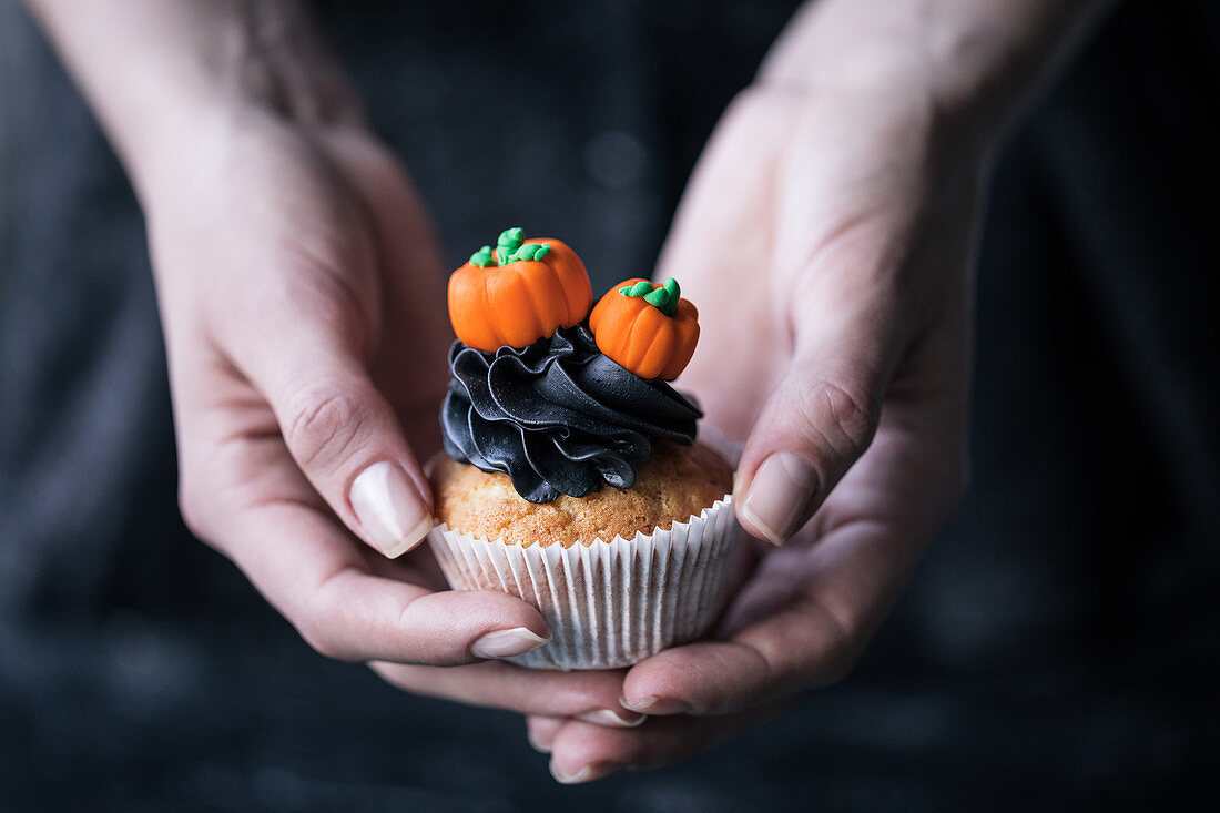 Hände halten einen Halloween-Cupcake