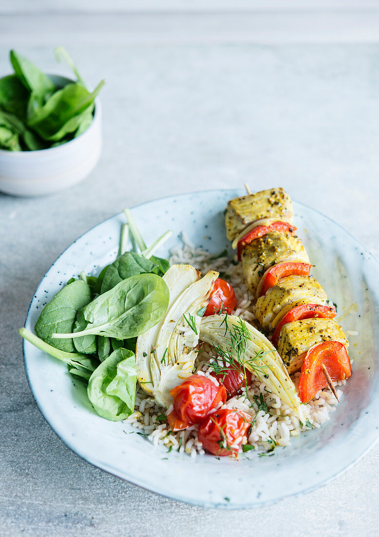 Spicy fish skewer with rice, cherry tomatoes, fennel and fresh spinach