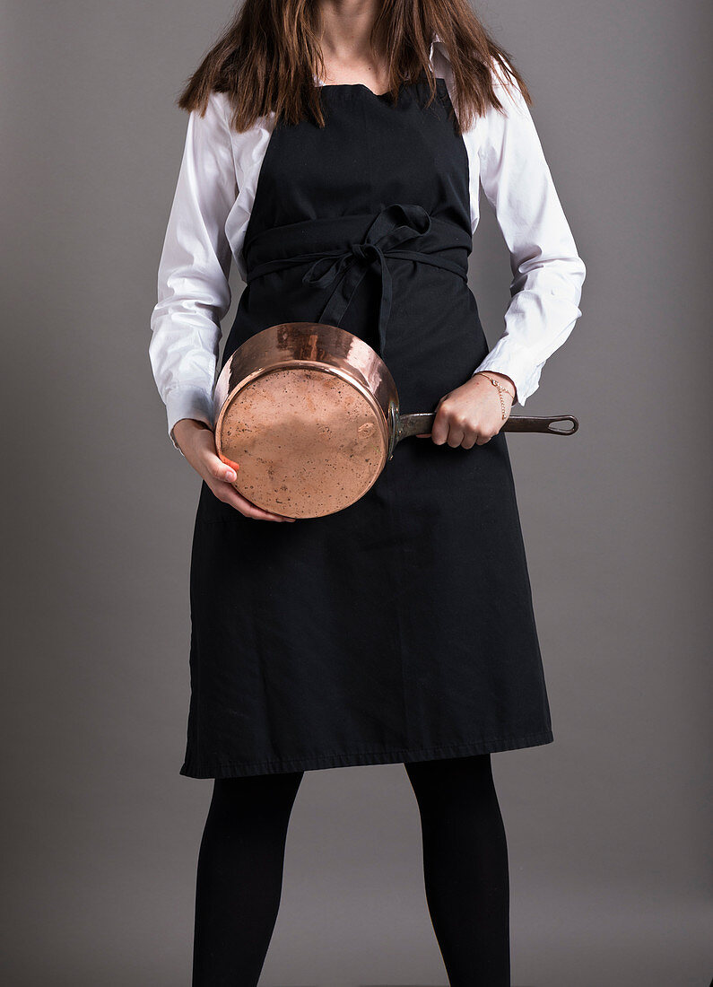 Woman wearing an apron holds a copper pot in her hands