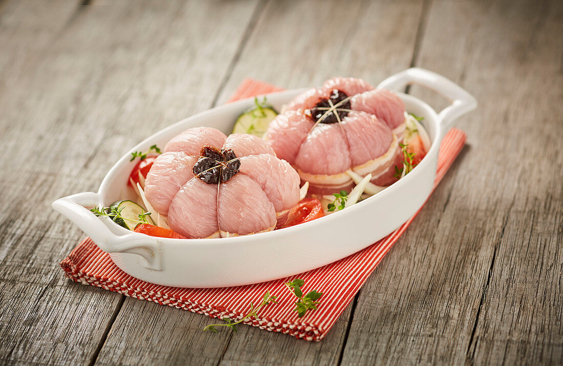 Raw poultry paupiettes wrapped in bacon on a bed of vegetables