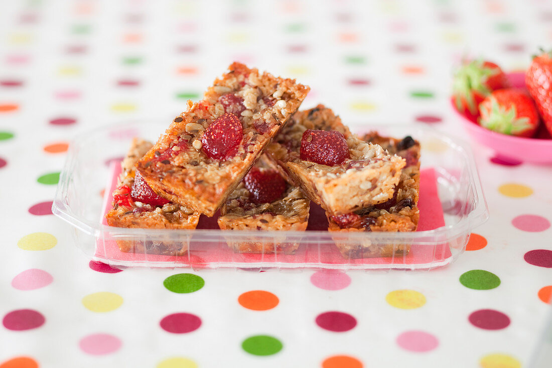 Muesli bars with strawberries in a plastic bowl on a dotted tablecloth