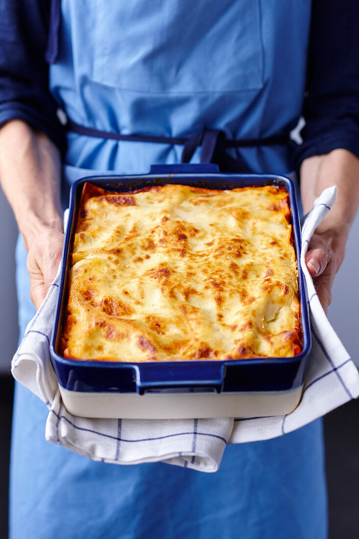 A person holding a baking dish with freshly baked lasagne