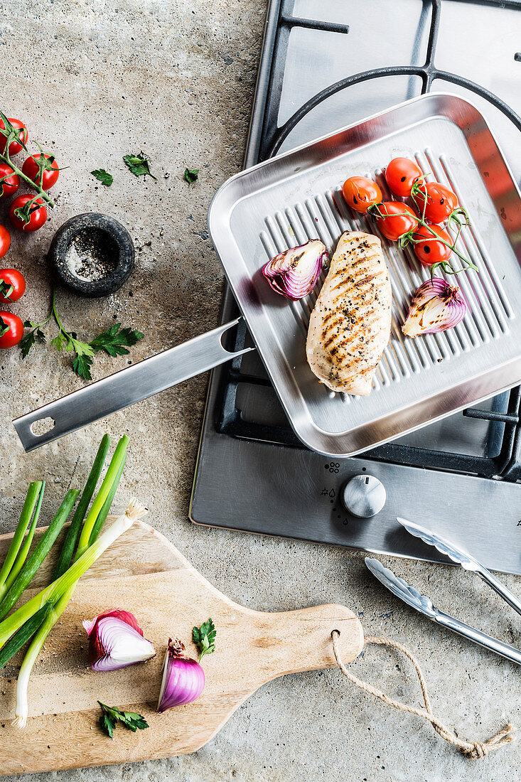 Grilled chicken fillet with cherry tomatoes and red onions on a grill pan