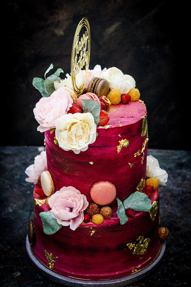 Two-tier red birthday cake decorated with flowers and macarons