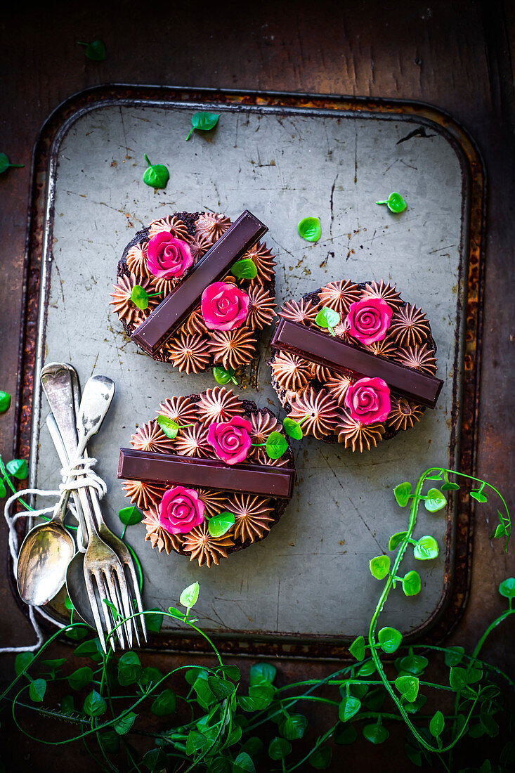 Mini-Brownie-Käsekuchen verziert mit Schokoriegeln, Cremetupfen und Rosenblüten