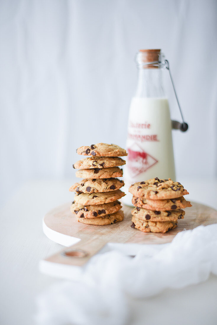 Chocolate chip cookies on a wooden board behind a milk bottle