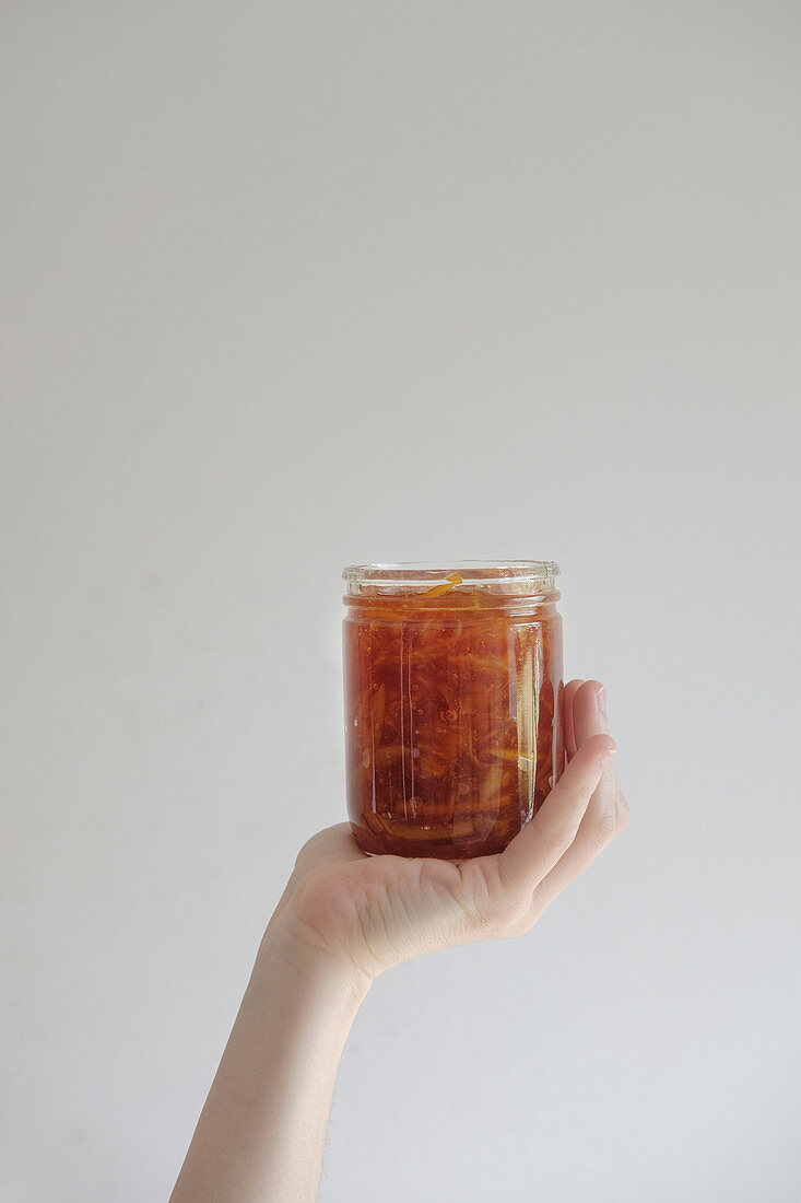 Hand holding a glass jar of orange marmalade