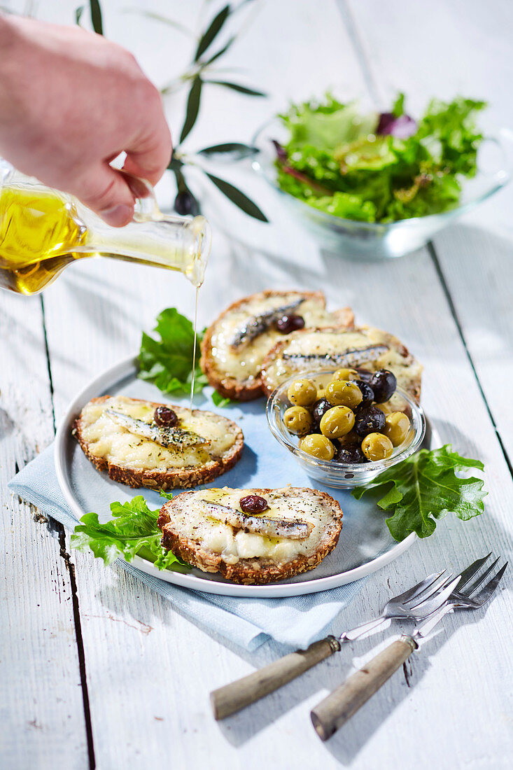 Olive oil drizzled on tartine with cheese, herring and olives