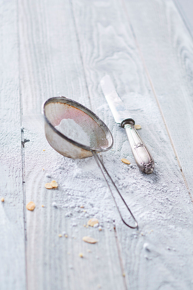 Sieve, icing sugar and a vintage knife on a wooden background