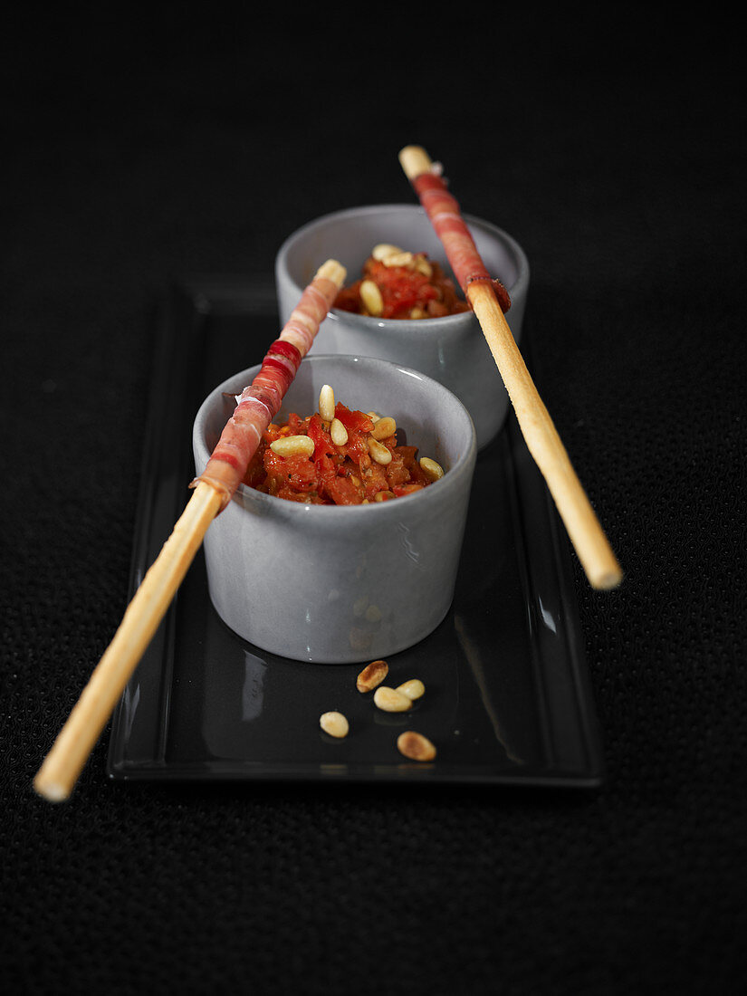 Candied tomato dips with pine nuts and breadsticks with cured ham